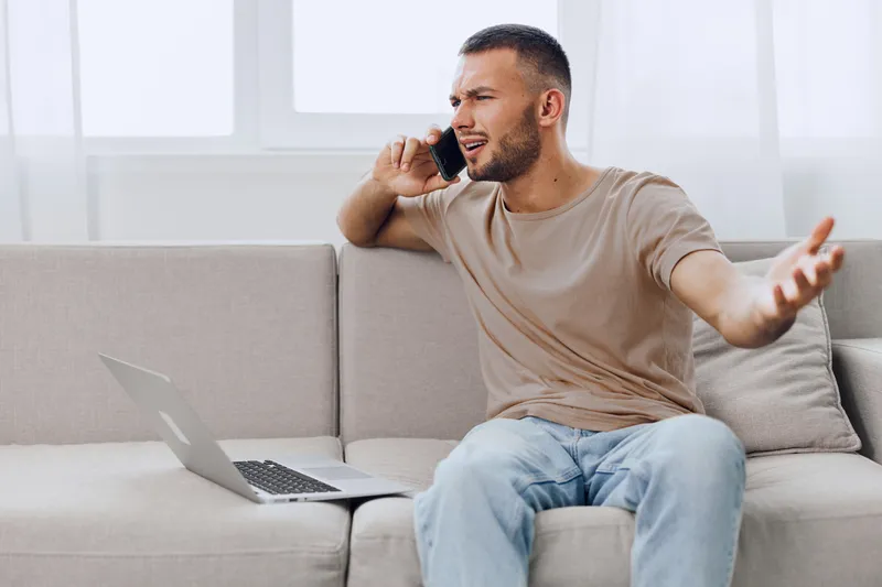 Frustrated man communicating on phone during a digital detox, expressing vulnerability while balancing remote work and personal life challenges.