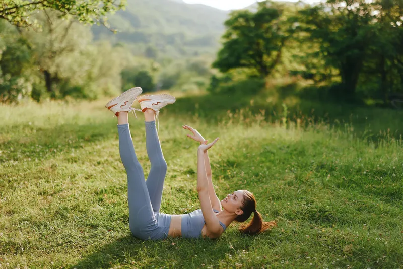 Young woman practicing yoga outdoors on green grass in bright athletic wear, showcasing flexibility and wellness in natural settings