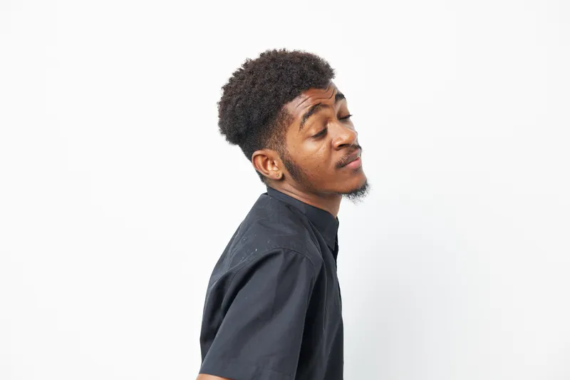 Confident black man with a stylish haircut, exuding charm and style. His expression reflects confidence and self-assurance in a minimalistic setting.