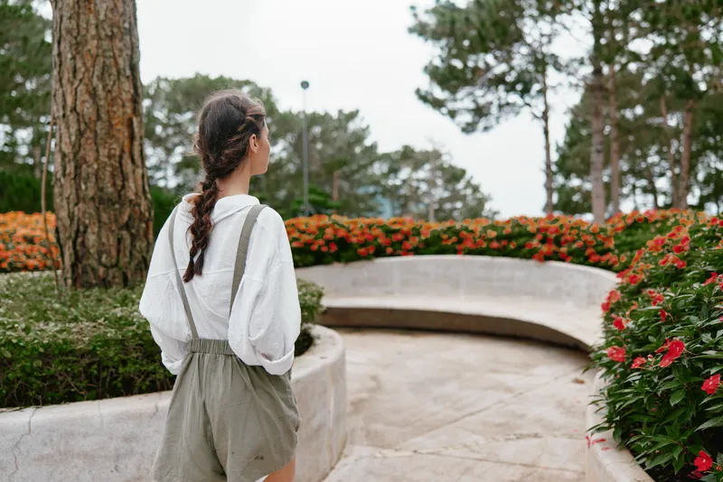 Young woman in casual outfit walking through a vibrant flower garden, surrounded by colorful blooms and greenery, conveying a sense of serenity and connection with nature