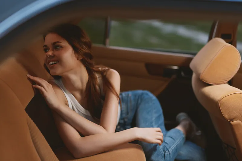 Young woman relaxing in a vintage car, wearing casual attire, expressing joy and comfort, perfect for lifestyle and travel themes.