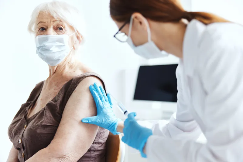 Пожилая женщина с врачом, держащим шприц с вакциной для защиты иммунитета
