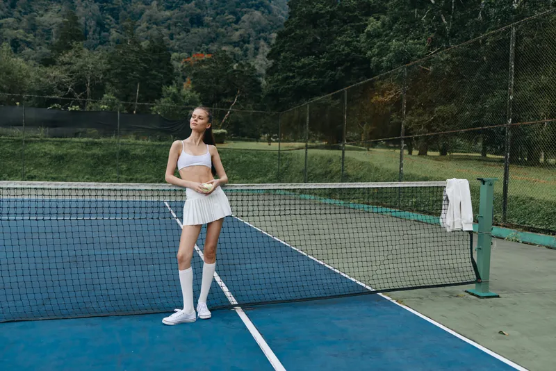 Young woman in stylish tennis outfit smiling on court, showcasing athleticism and confidence in a vibrant green setting, perfect for sports and fitness concepts