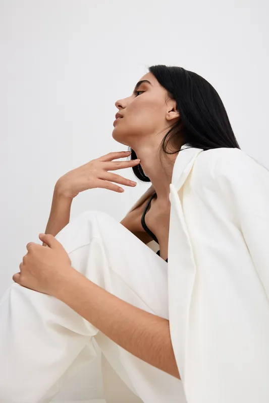 thoughtful woman in white suit posing in studio, dark hair, minimalist style, soft lighting, modern fashion, calm expression, neutral background