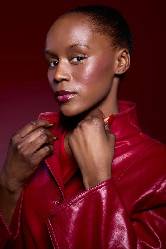 Portrait of a confident dark skinned African woman wearing a red leather jacket on a dark red background. Concept of fashion, beauty, empowerment, and style with studio lighting.
