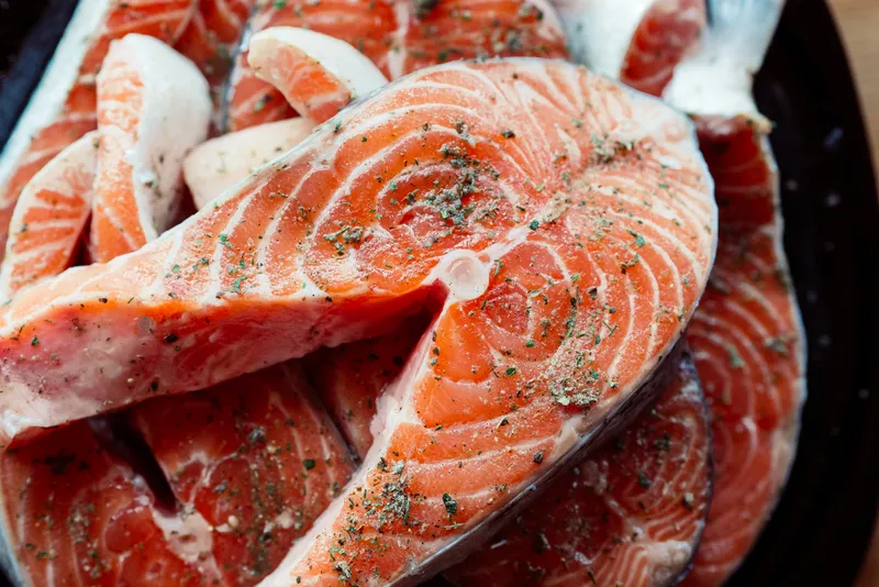 Нарезанная красная рыба на тарелке, приготовление морепродуктов на деревянном фоне