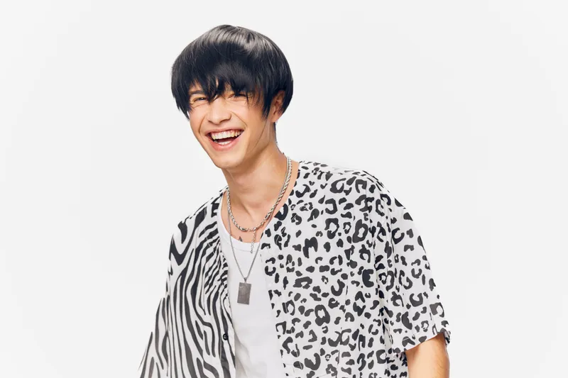 smiling young man wearing black and white animal print shirt on white background expressing joy and happiness in casual style