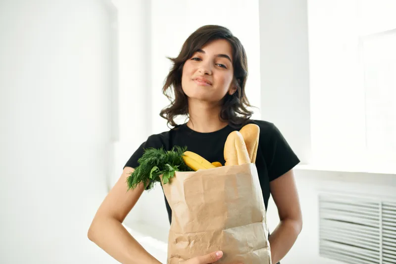Весёлая женщина с пакетом продуктов и овощей