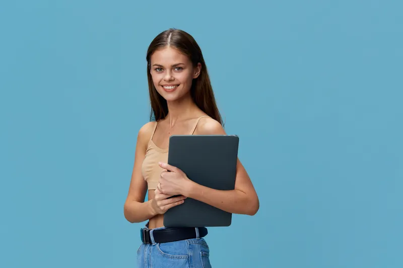 young woman holding laptop smiling white casual clothing blue background bright cheerful confident technology concept