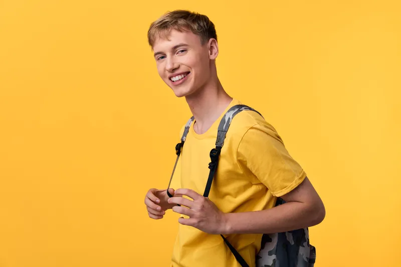 Smiling young man with backpack in a bright yellow studio, casual attire, education themed lifestyle shot, suitable for school, campus, or e learning promotions.