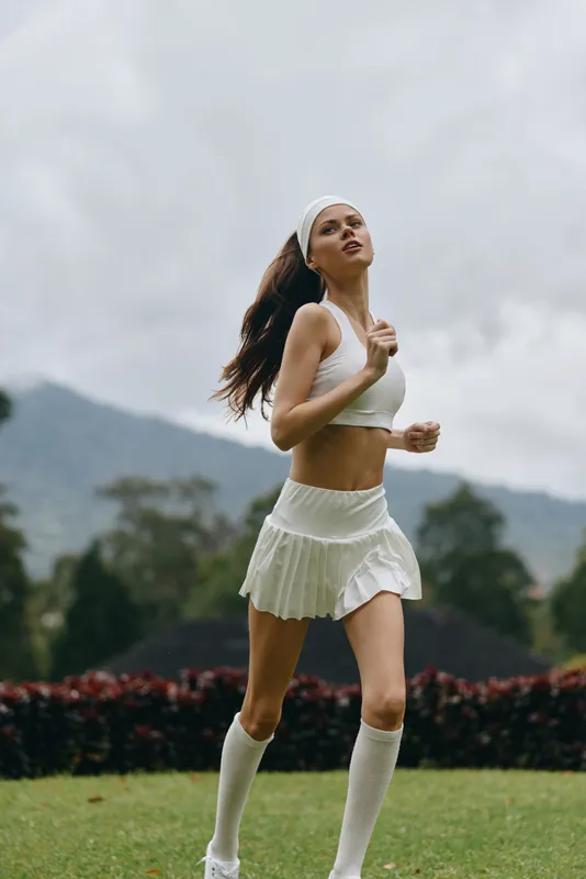 Young athletic woman running outdoors in a white sports outfit against a natural backdrop, conveying health and fitness, joy, and dynamism
