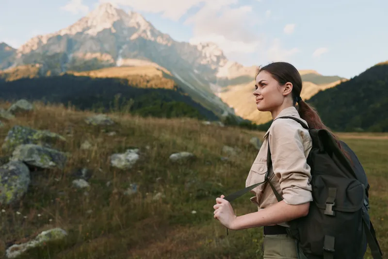Young woman hiking outdoors with backpack, enjoying mountain view, casual clothing, natural light, peaceful atmosphere, active lifestyle, scenic landscape background