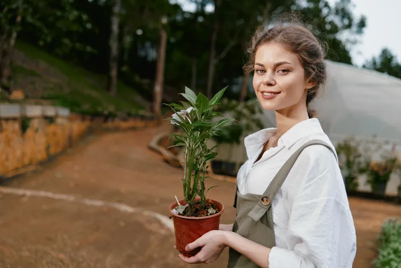 Young woman holding a potted plant in a natural setting, showcasing a connection to nature, sustainable living, and gardening enthusiasm