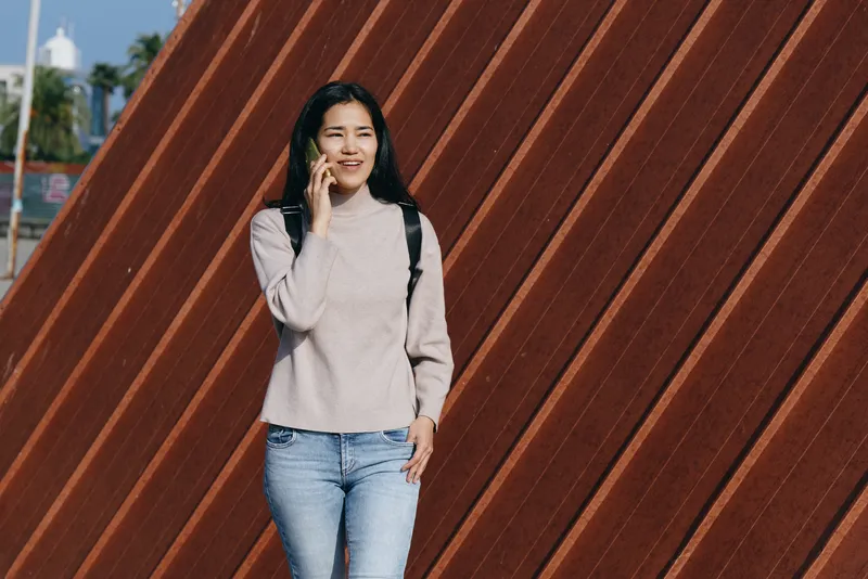 Woman talking on phone in casual jeans outfit beside an angled wooden wall, outdoor urban setting, daylight, cheerful vibe, lifestyle and fashion in a candid moment