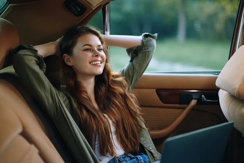 Relaxed young woman enjoying her time in a vintage car, embodying peace and serenity through her smile and casual outfit, perfect for lifestyle and travel themes.
