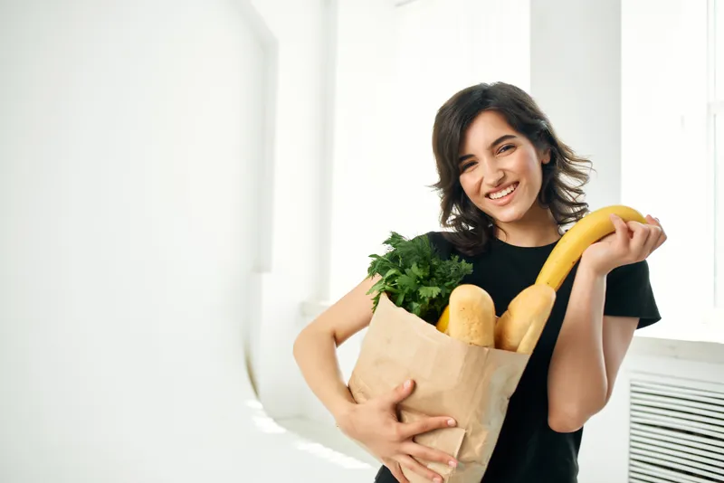 Женщина в черной футболке распаковывает продукты из супермаркета и готовит