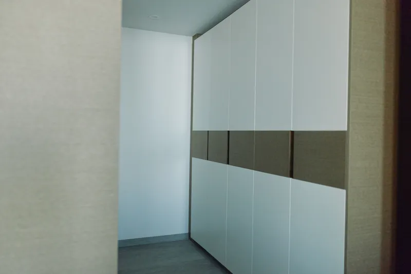 Minimalist hallway with tall white cabinets and dark horizontal band, clean lines, organized storage space, modern interior, sleek furniture, quiet corridor, spacious feel with neutral tones