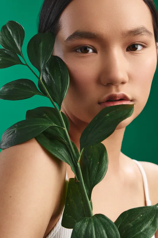 asian woman close to a green leafy plant in a studio portrait, her calm expression and soft lighting evoke natural beauty and serene focus.
