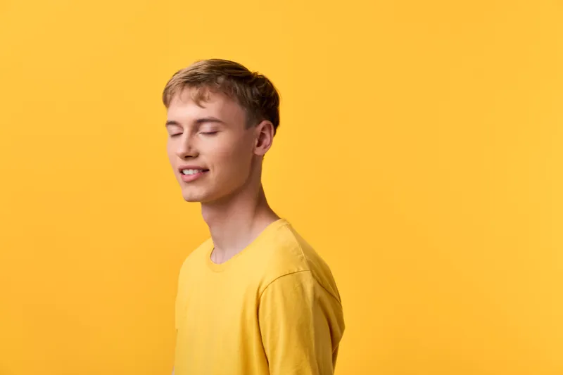Yellow clad man with eyes closed stands against a bright yellow backdrop, conveying calm, simplicity and warm mood ideal for lifestyle, wellness, fashion and color themed campaigns