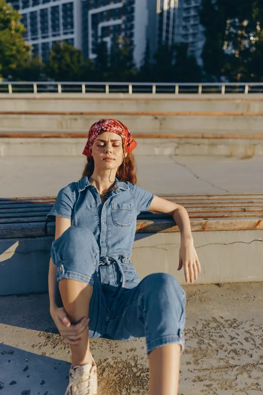 Relaxed lifestyle woman in modern boho-western denim outfit sitting outdoors on steps in warm natural light, film color style conveying casual urban street fashion.