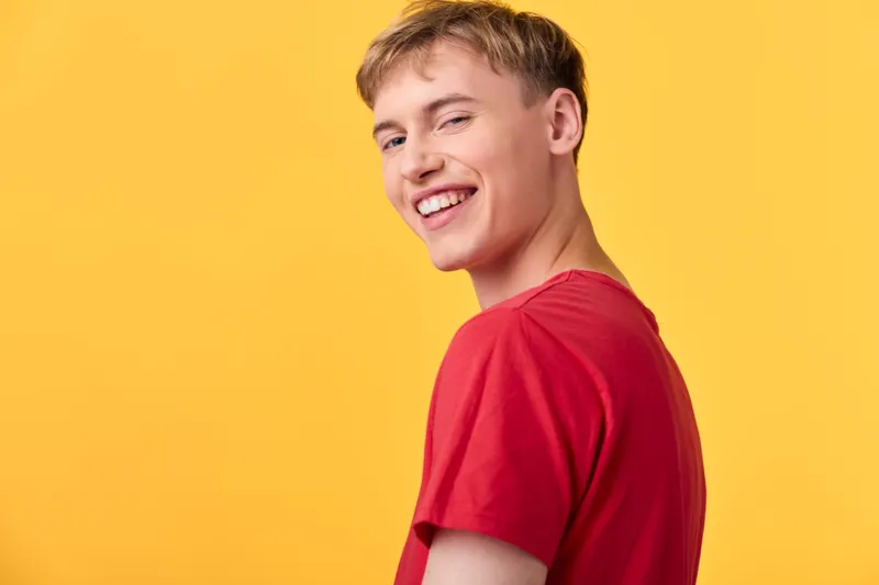 Smiling man in a red shirt stands before a vibrant yellow backdrop, casual lifestyle photo with bright color, clear lighting, and a cheerful mood suitable for positive branding