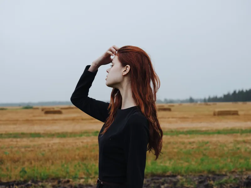 Красивая женщина в чёрном платье идёт по полю на природе осенью
