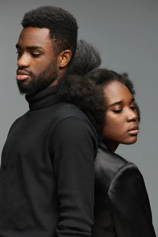 Stylish young couple with natural Afro hairstyles and elegant dark clothing, showcasing confidence and modern aesthetics against a neutral background