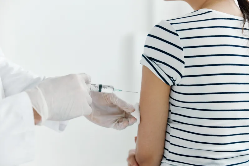 Врач в медицинских перчатках делает инъекцию вакцины в руку пациента крупным планом