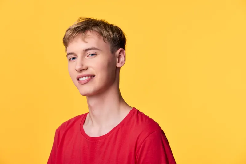 Young man smiling in a red shirt against a bright yellow backdrop, casual studio setting ideal for lifestyle, fashion, advertising campaigns and social media content