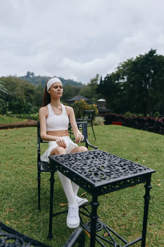 Young female model in sporty outfit, expressing calmness outdoors, surrounded by greenery and elegant furniture, perfect for healthy lifestyle themes
