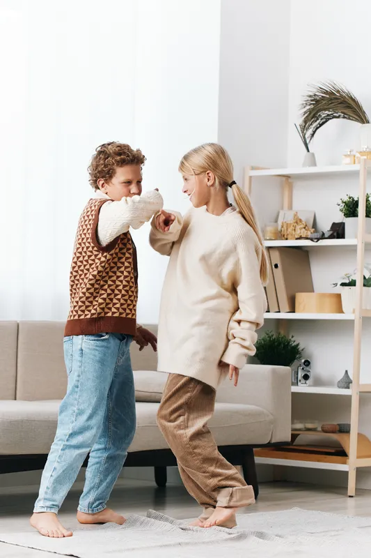 Two adults dancing indoors in cozy sweaters, barefoot on a soft rug, embracing playful movement and warm light in a bright modern living room with calm atmosphere.
