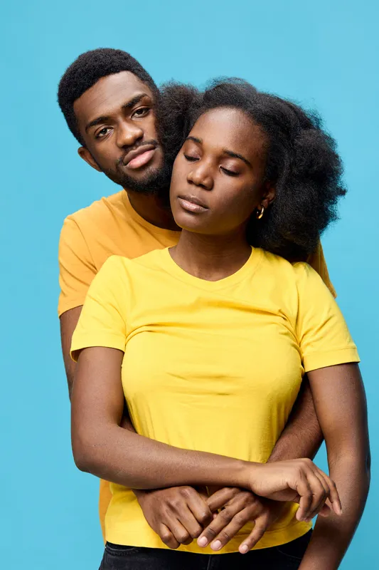 Affectionate couple embracing against a bright blue background, showcasing love and connection through emotions in vibrant yellow and orange t shirts