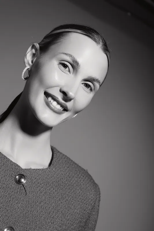 Smiling caucasian woman with fair skin and sleek hair poses in elegant outfit and hoop earrings. Studio portrait in black and white with soft lighting and smooth background.