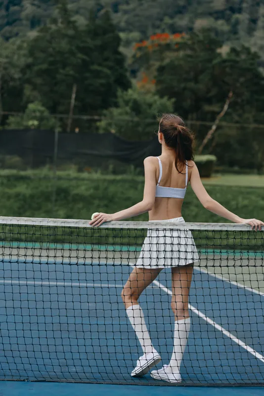 Young athletic woman in sportswear stands at a tennis court, showcasing a confident pose and a healthy lifestyle, perfect for tennis themed content