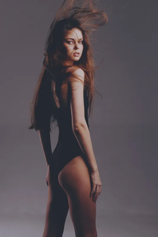 Woman with long hair wearing black bodysuit posing with wind effect, fashion, elegance, portrait mood