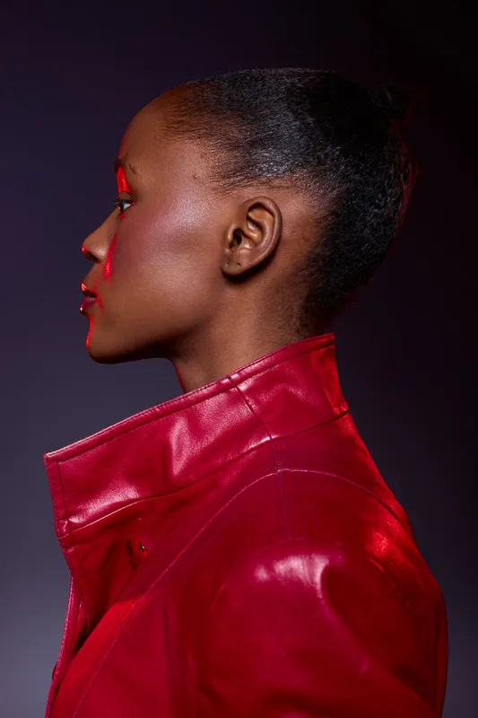 Profile of an African American woman with dark skin wearing a red leather jacket. Studio portrait with dramatic lighting and black background. Concept for fashion and style.