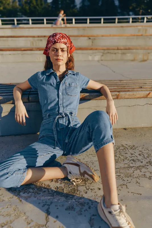 lifestyle woman wearing modern boho-western denim outfit sitting outdoors in street style with film color tones and relaxed confident pose