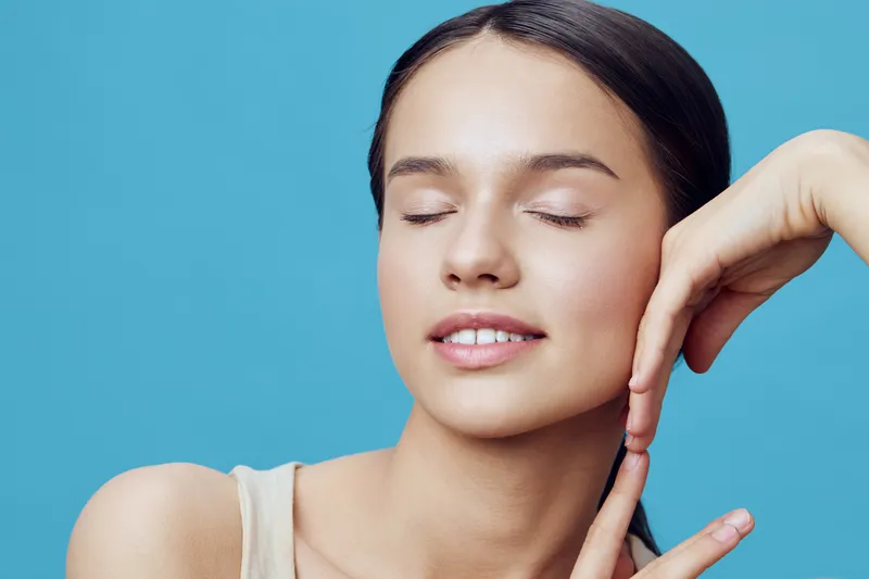 Young woman with closed eyes smiling gently against a soft blue background, showcasing tranquility and beauty in a minimalistic style Emphasizing a serene emotion