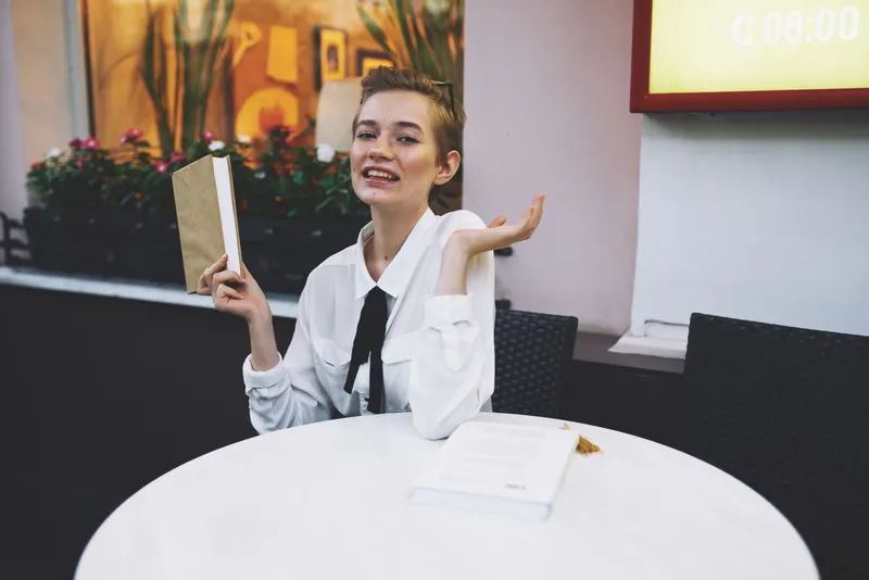 Женщина с короткой стрижкой читает книгу, которую держит в руках