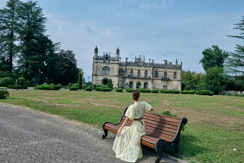 woman on bench in park facing mansion, wearing vintage dress, architecture backdrop, reflective moment with authenticity and inclusivity in travel life