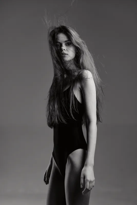 Black and white portrait of a young woman in a black sleeveless outfit with long hair and a serious expression.