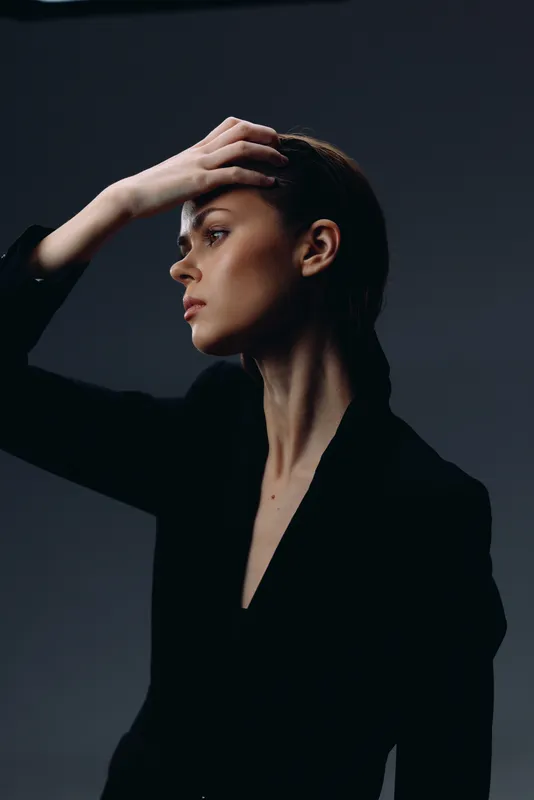 Profile of a thoughtful woman in black clothing with a dark moody background and minimal lighting.