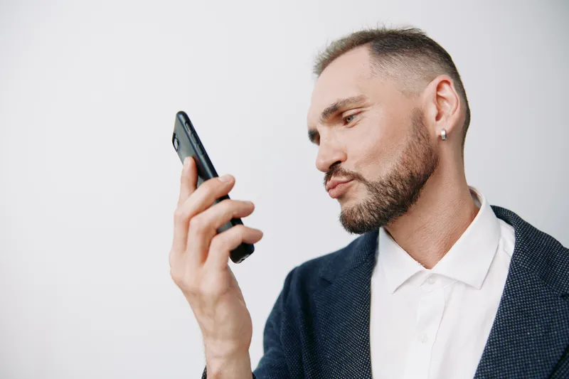 A professional man in business attire speaks into a smartphone, displaying focused emotions and confident demeanor against an isolated neutral background.