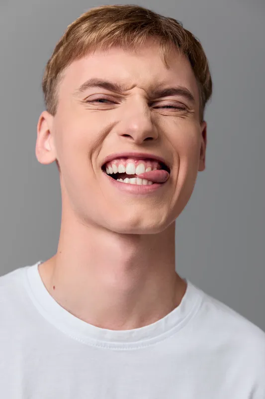 Closeup of a man with a playful grimace, conveying joy and humor. Studio lighting, casual white tee, cheerful expression and candid mood with a vibrant, energetic vibe