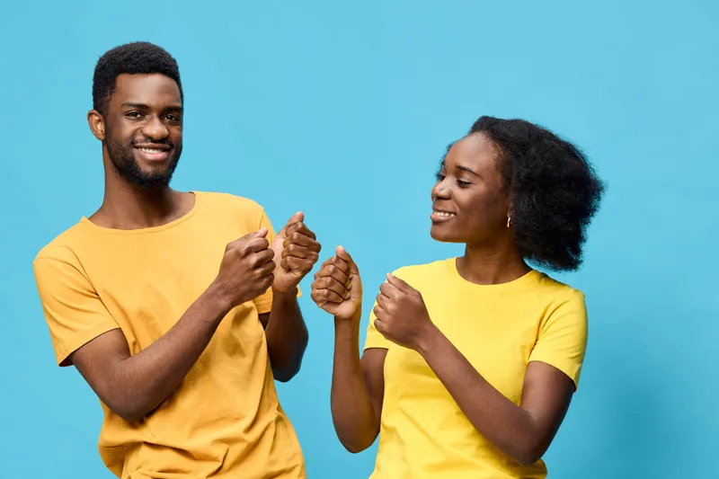 Joyful young African couple wearing matching yellow t shirts dancing against a blue background, expressing happiness and connection through movement and smiles