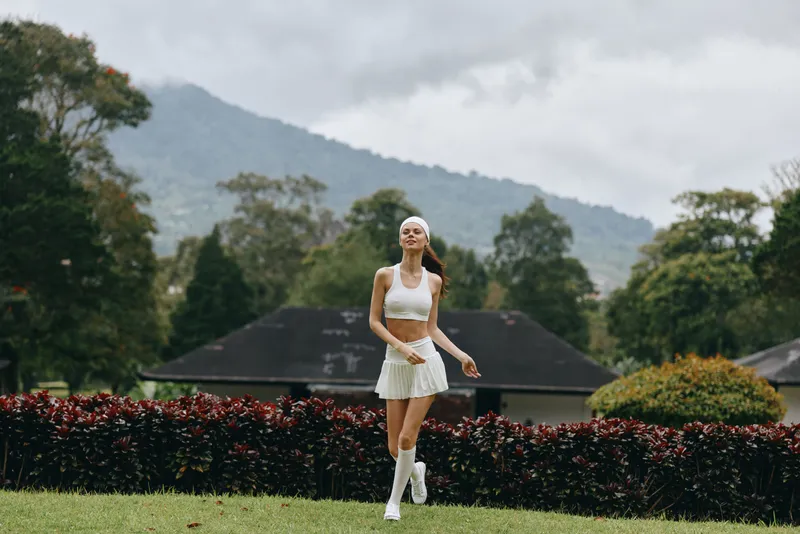 Young woman in white sportswear walking in a lush green park, expressing joy, ideal for fitness and healthy lifestyle themes