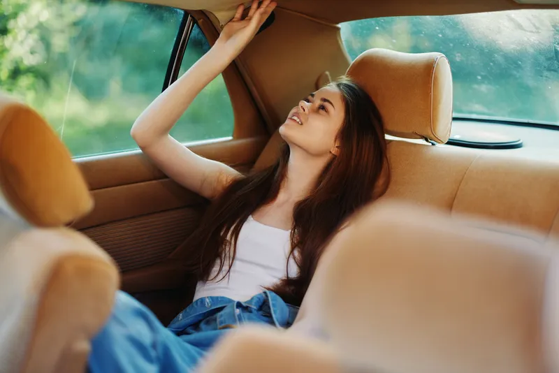 Young woman relaxing in the backseat of a car, enjoying the moment in a casual outfit with a serene expression, surrounded by soft colors and natural light.