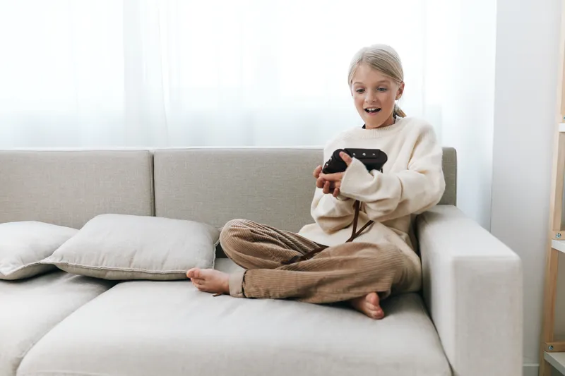 Authenticity shines as a young student enjoys a playful moment at home, using a handheld device on a cozy couch, blending study focus with casual lifestyle.
