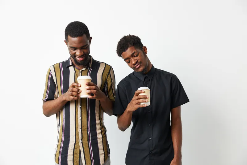 Two smiling black men enjoying coffee together, showcasing friendship and connection in a comfortable setting. Concept: warmth and joy.