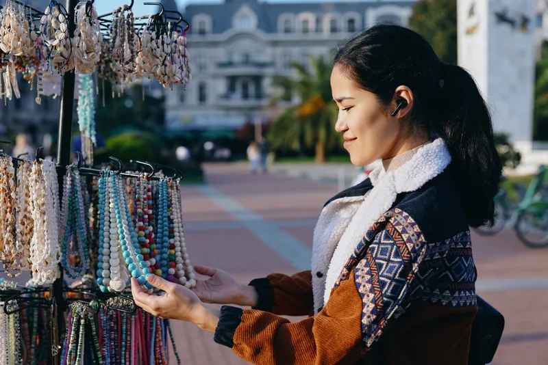 Jewelry display with colorful bead necklaces and bracelets as a shopper browses at an outdoor market, capturing craft, style, and street commerce in a bright, sunlit scene